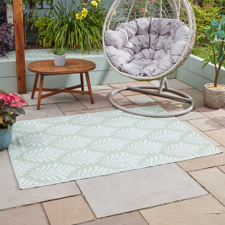 leaf patterned green and white outdoor rug on patio tiles