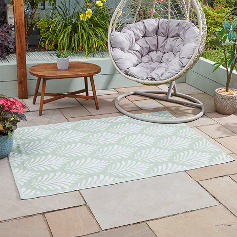 leaf patterned green and white outdoor rug on patio tiles