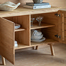 close up on inside of light oak sideboard, two doors open to show four shelving spaces with crockery and glassware inside