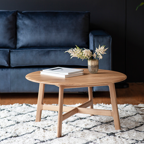 round solid oak coffee table on top of a checked white and blue fluffy rug, with navy blue sofa in the background