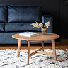 round solid oak coffee table on top of a checked white and blue fluffy rug, with navy blue sofa in the background