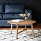 round solid oak coffee table on top of a checked white and blue fluffy rug, with navy blue sofa in the background
