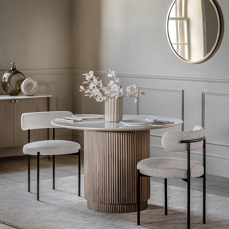 image of round ribbed fluted mango wood dining table with marble tabletop, on cream rug of dining table and two modern chairs tucked on either side of it