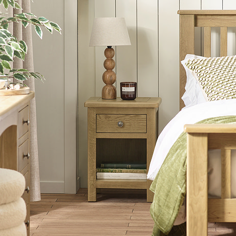 image of 1 drawer solid oak bedside table with bottom shelf, topped with bobble lamp and candle, next to matching bed