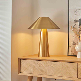 image of brushed brass colour table lamp on light oak console table, emitting warm light of bulb within