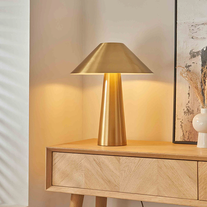 image of brushed brass colour table lamp on light oak console table, emitting warm light of bulb within