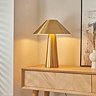 image of brushed brass colour table lamp on light oak console table, emitting warm light of bulb within