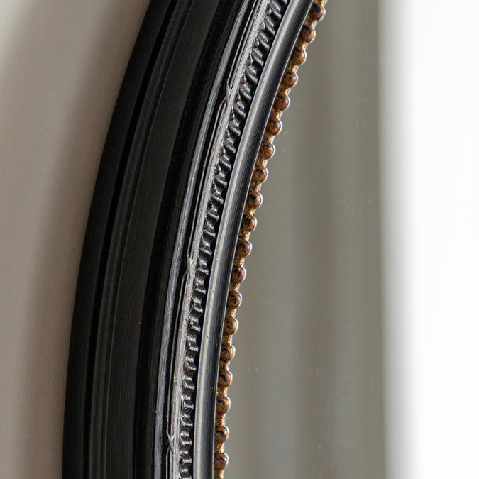 close up image of black round wall mirror with gold inner trim detailing