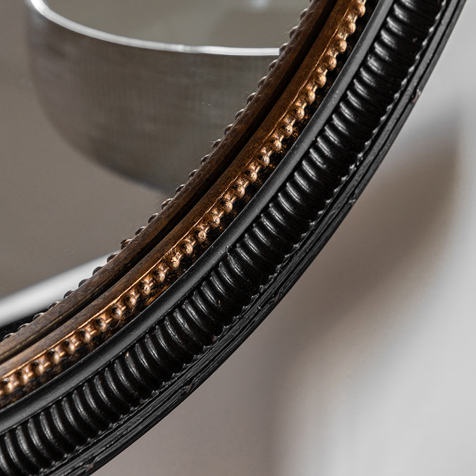 close up image of black round wall mirror with gold inner trim and bobble detail