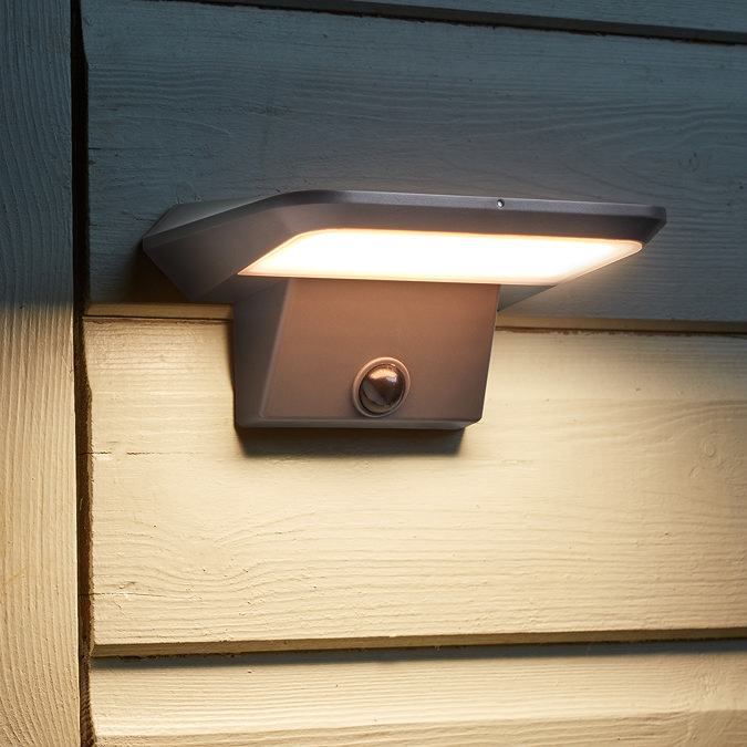 close up image of motion sensor security light attached to the outside of garden shed, emitting warm light