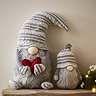 plush grey gonk next to larger grey gonk holding a red heart, both sat on a light wood mantlepiece