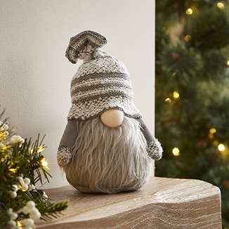 plush grey gonk santa on a wooden mantlepiece with christmas tree in background