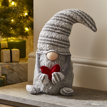 plush grey gonk with heart, sat next to smaller grey gonk on a light wood mantlepiece