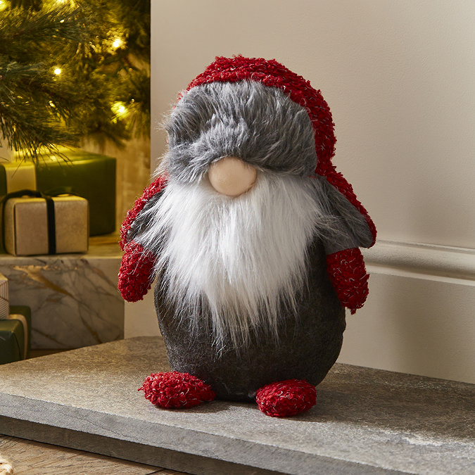 plush grey gonk santa with red wool hat sat on the hearth