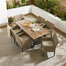 image taken from above of rectangular wooden garden table with six rattan chairs tucked around it, on stone patio