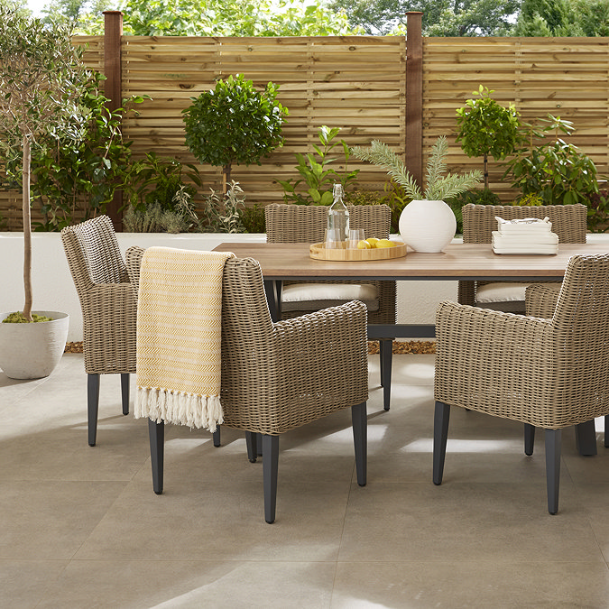 close up image on left side of garden dining set, rattan chairs under a wooden table, one chair with yellow throw draped over the back of it