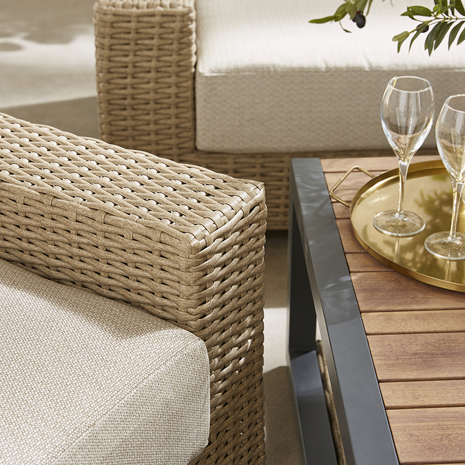 close up image on chunky rattan armchair and slatted wooden table of corner sofa set