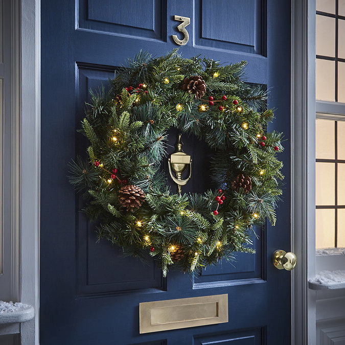 pre-lit green wreath with pine cones and cranberries, hung on a navy blue front door