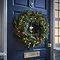 pre-lit green wreath with pine cones and cranberries, hung on a navy blue front door
