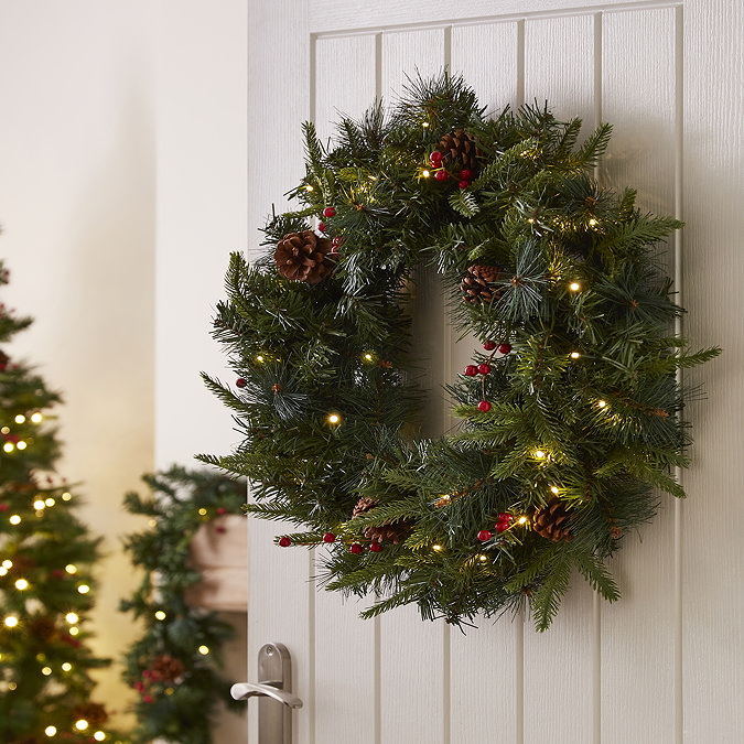 pre-lit green wreath with pine cones and cranberries, hung on the back of a white wooden living room door
