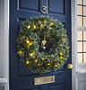 pre-lit pine wreath with warm white LEDs hung on a navy blue front door
