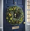 pre-lit pine wreath with warm white LEDs hung on a navy blue front door