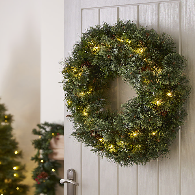 pre-lit pine wreath hung on the back of a white wooden living room door