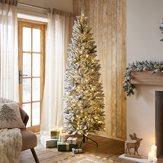 pre-lit slim snowy spruce tree in middle of warmly lit living room