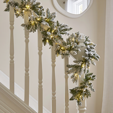 close up image of snowy garland with warm white LEDs draped across a light oak mantlepiece