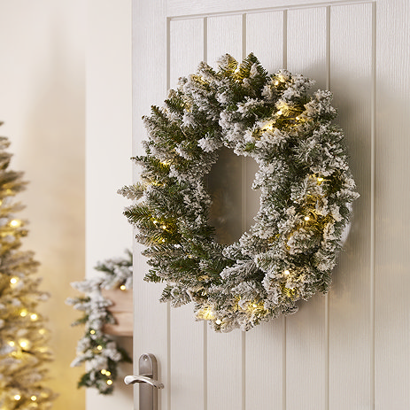 pre-lit snowy spruce christmas tree, hung on the back of a white wooden living room door.