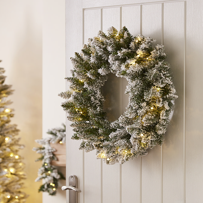 pre-lit snowy spruce christmas tree, hung on the back of a white wooden living room door. 