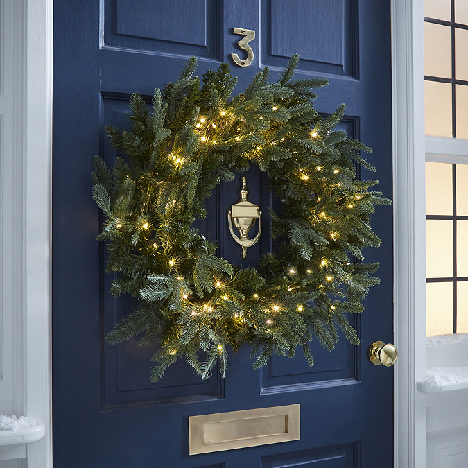 pre-lit green wreath with 100 LEDs, hung on a navy blue front door at night