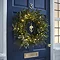 pre-lit green wreath with 100 LEDs, hung on a navy blue front door at night