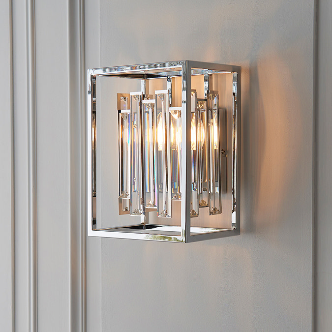 image of cubed chrome metalwork wall light with bevelled glass sides on a grey wall emitting warm light