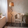 image of black wriggle shaped floor lamp with raffia shade, emitting warm glow in corner of living room