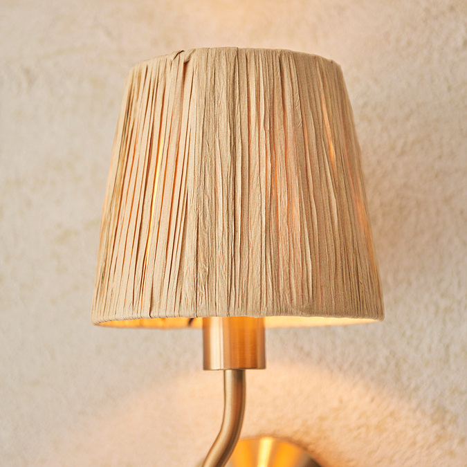 close up on raffia shade of brushed brass wriggle wall light, emitting warm glow