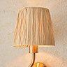 close up on raffia shade of brushed brass wriggle wall light, emitting warm glow