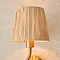 close up on raffia shade of brushed brass wriggle wall light, emitting warm glow