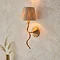 side on image of brushed brass wriggle light with raffia shade on cream wall