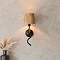 image of black wriggle wall light with raffia shade on a cream wall emitting a warm glow
