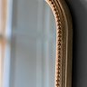 close up image of rounded top of large wall mirror, focused on the beaded detail of the champagne-coloured frame
