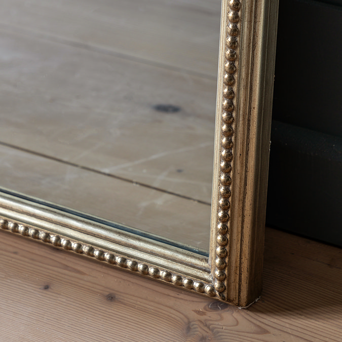 close up on bottom of champagne-coloured mirror with beaded detailing, resting on wooden floor panels