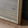 close up on bottom of champagne-coloured mirror with beaded detailing, resting on wooden floor panels