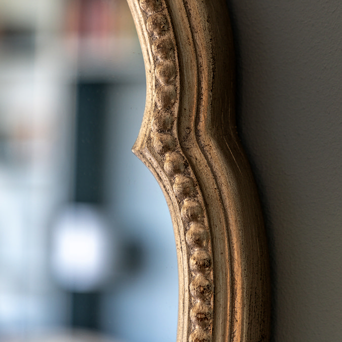 close up image on right side of champagne gold rounded wall mirror, focus on beaded edge detail