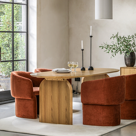 image of curved light oak veneer dining table with rust coloured sofa chairs surrounding it. topped with candles and plates
