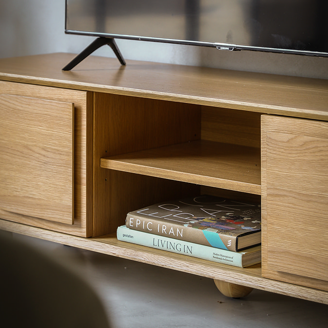 close up on middle part of oak tv unit, open to show two shelves where two books rest on the bottom shelf