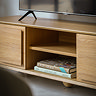 close up on middle part of oak tv unit, open to show two shelves where two books rest on the bottom shelf