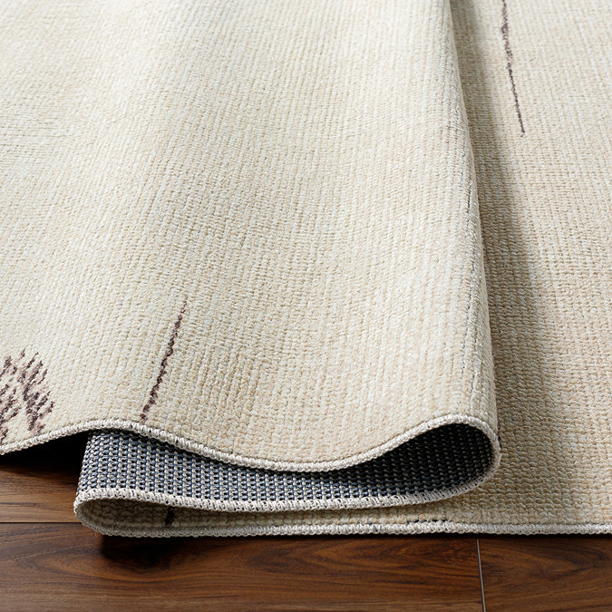 close up image of cream rug with asymmetrical charcoal boho line pattern, ruched up slightly to show its thinness
