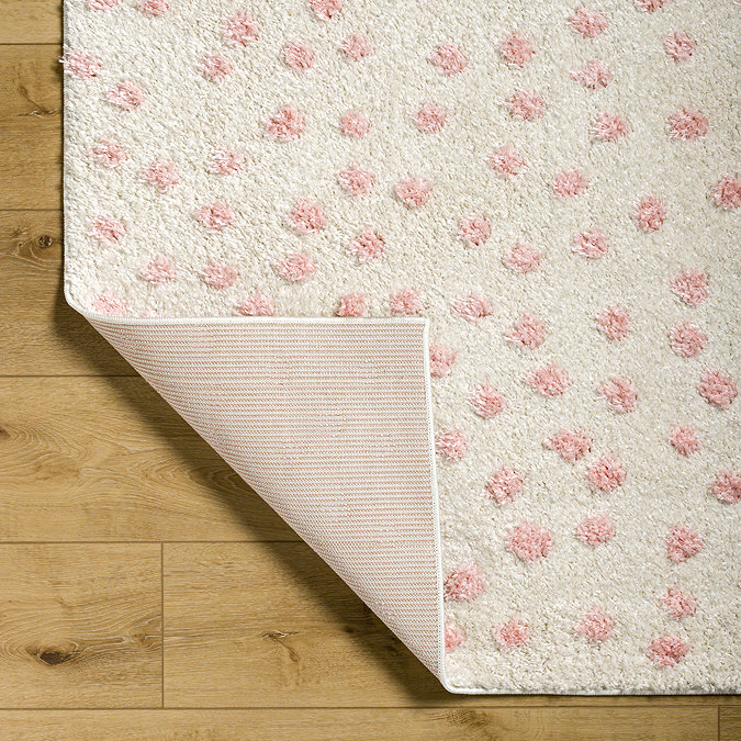 close up image on corner of cream rug with pink spots, folded over at edge to show reverse material