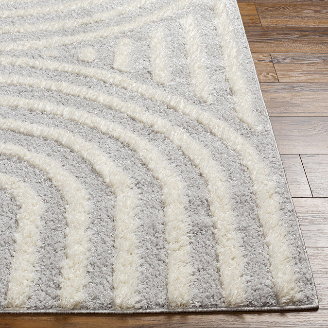 close up on corner of soft grey rug with arch line pattern, on light wood flooring